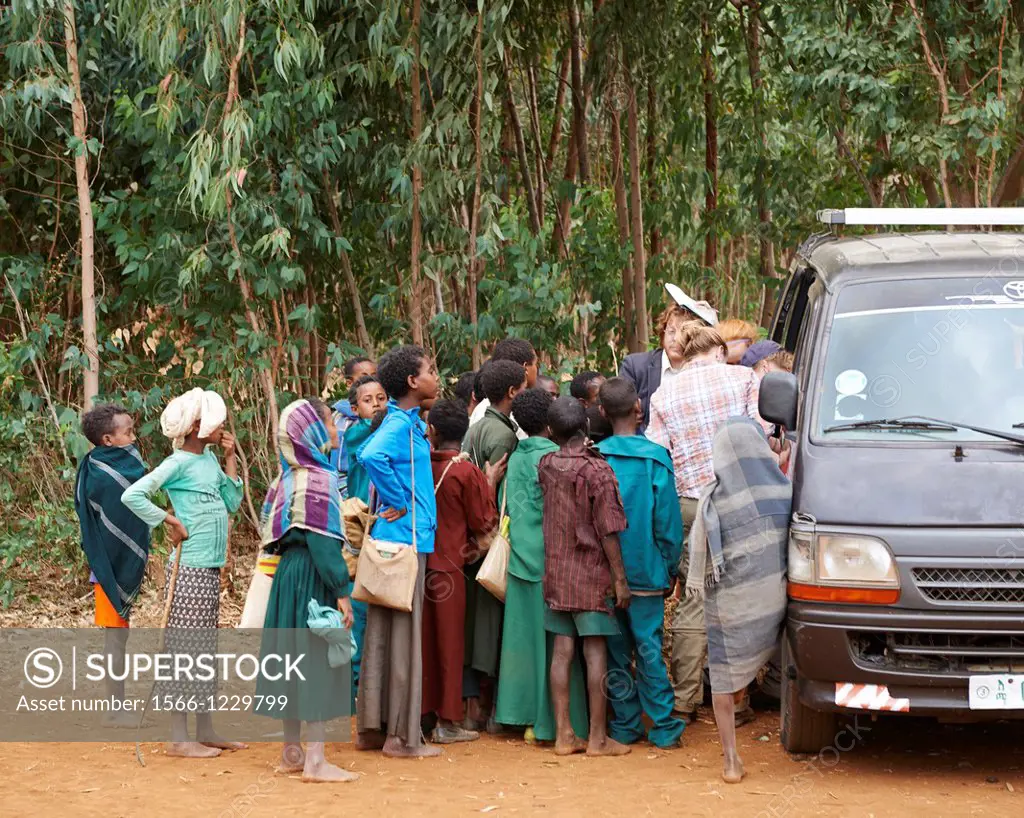 A group of children crowd a mini van on a dirt road