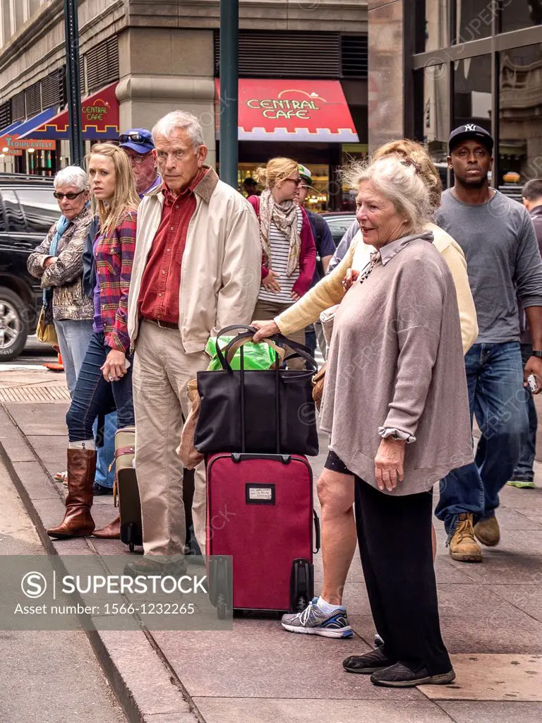 A grim-looking group of newly-arrived travelers wait on the sidewalk outside New York´s Grand Central Station with their luggage for taxi transportati...