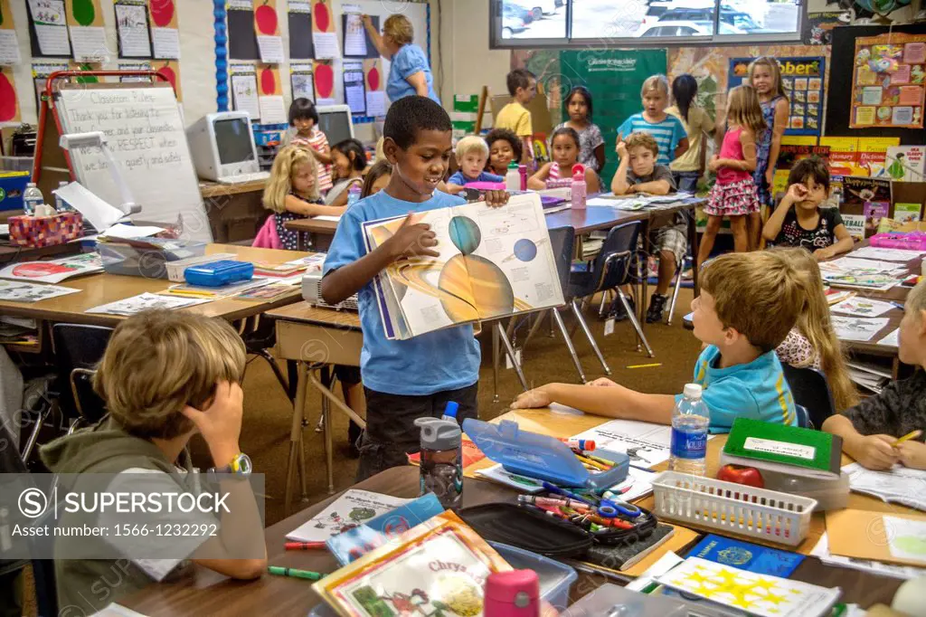 An African American elementary schoolboy uses an illustrated astronomy book to explain the Solar System to his classmates in Laguna Niguel, CA