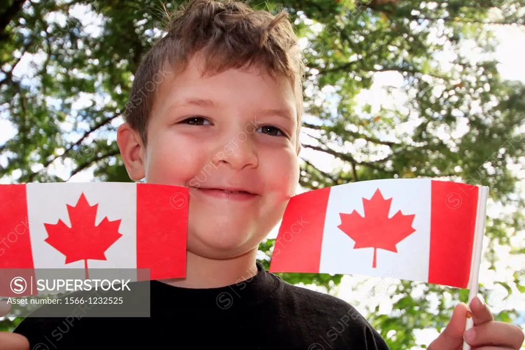 a five year old boy holding up Canadian flags in celebration of Canada Day July 1st in Canada