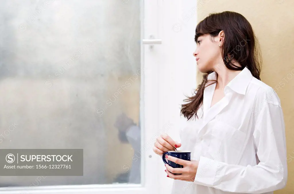Pensive brunette woman with coffee looking out the window