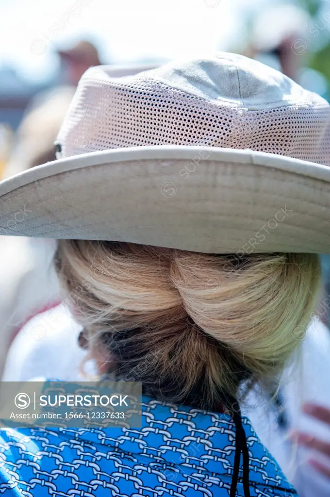 Partial back view of a woman´s head with blond hair in a braid and a cloth hat.