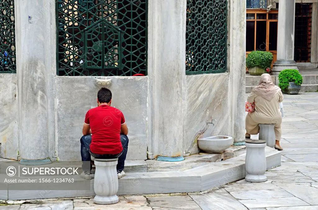 Man in modern dress and woman in traditional dress at the water taps, Blue Mosque, Istanbul, Turkey, NMR.