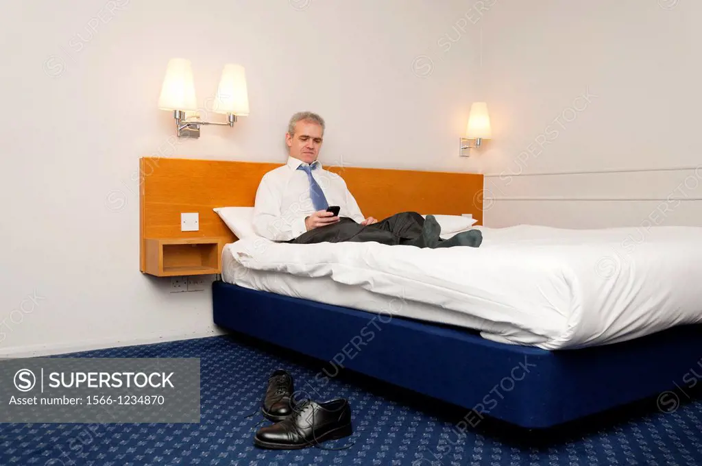 Business man sitting on hotel bed checking his phone for messages