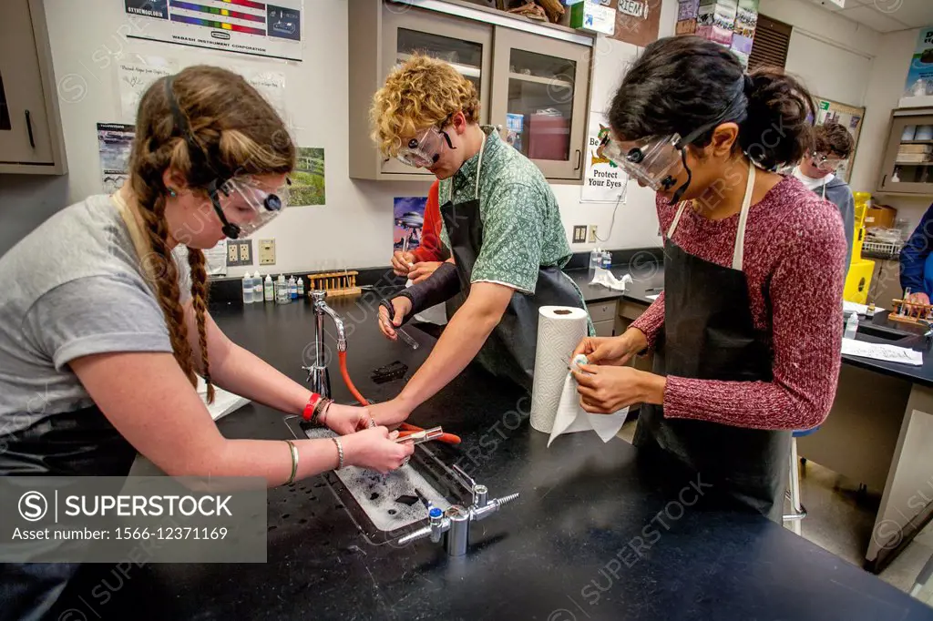Multiracial high school chemistry students wash laboratory glassware after an experiment in San Clemente, CA. Note safety goggles and aprons.