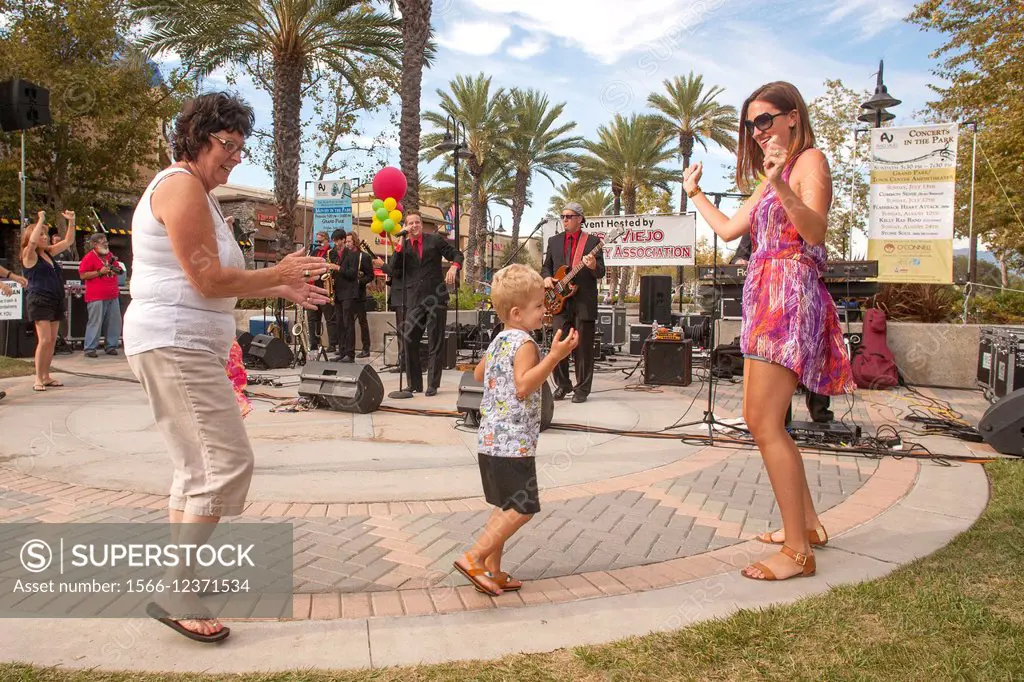 Three generations of a family dance to a live band at an evening outdoor concert in an Aliso Viejo, CA, public park.