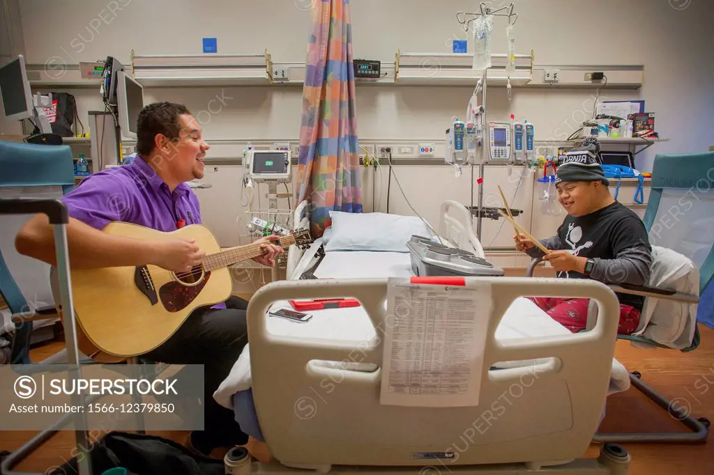 A music therapist playing a guitar entertains a young boy patient at CHOC Children´s Hospital in Orange, CA. Note child playing on drums.