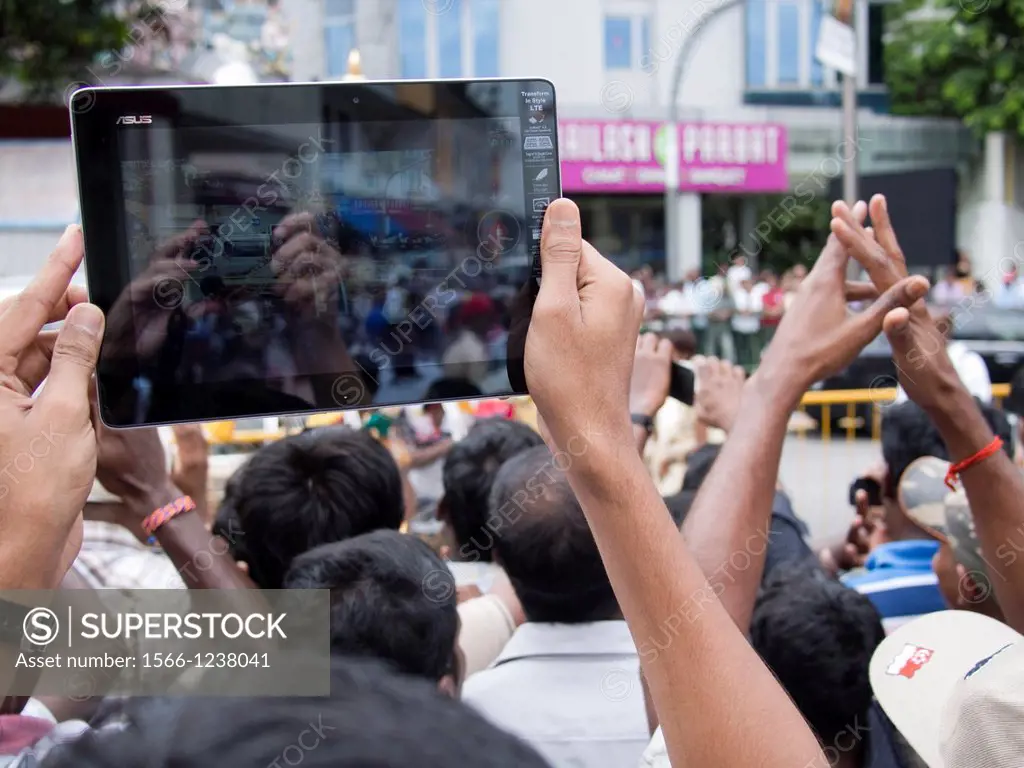 Human hand using tablet computer to photograph crowd gathered for a religious procession in Singapore