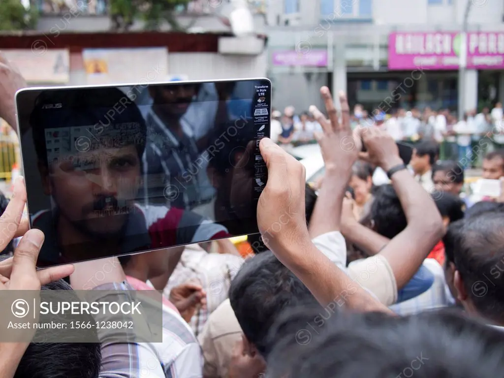 Human hand using tablet computer to photograph crowd gathered for a religious procession in Singapore