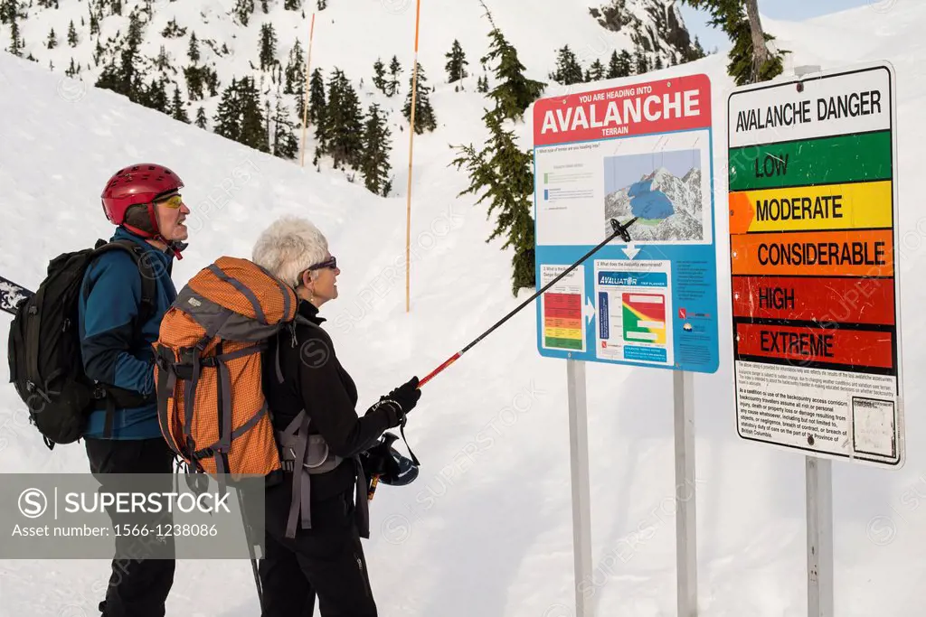 a middle-aged couple looks at the sign about avalanche danger on Mt Seymour, North Vancouver, BC, Canada