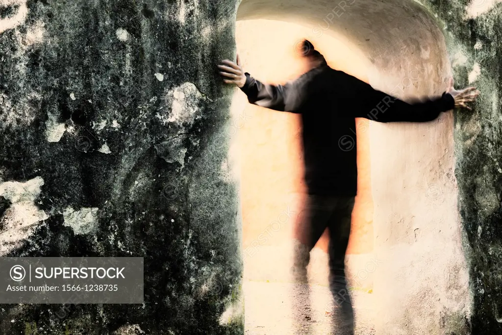 Adult male moving from darkness into light through portal  He is holding on to the stone wall