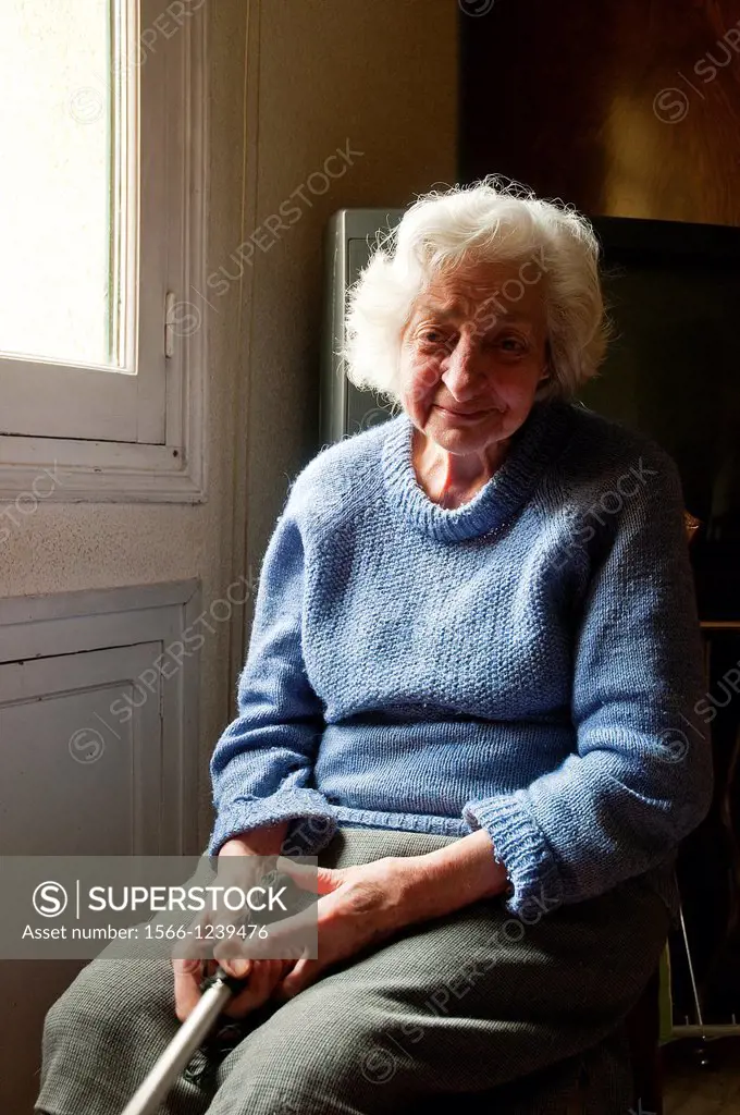 Portrait of old woman at home, sitting by the window, smiling and looking at the camera