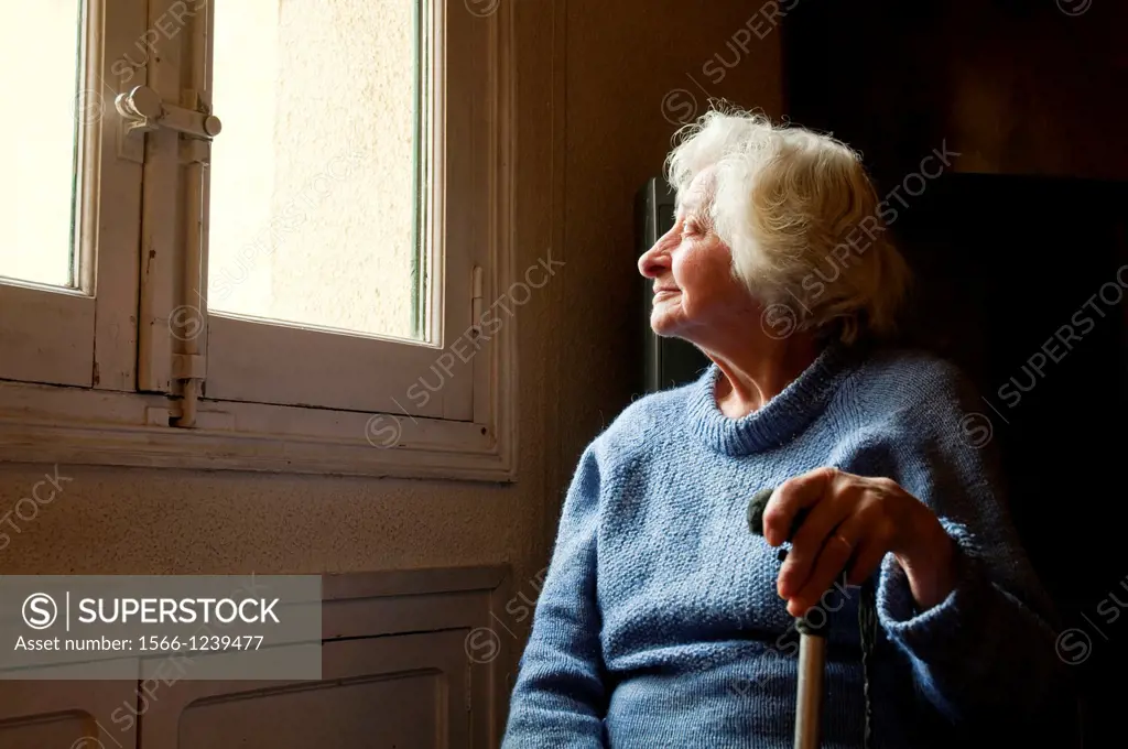 Portrait of old woman at home, smiling and looking at the window