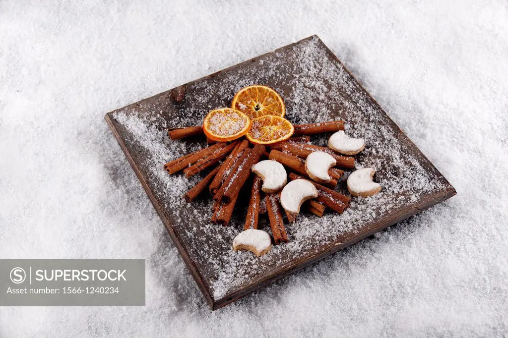 cinnamon sticks - dried orange slices - cinnamon halfmoon cookies at christmas - artificial snowflakes on potpourri in wooden bowl