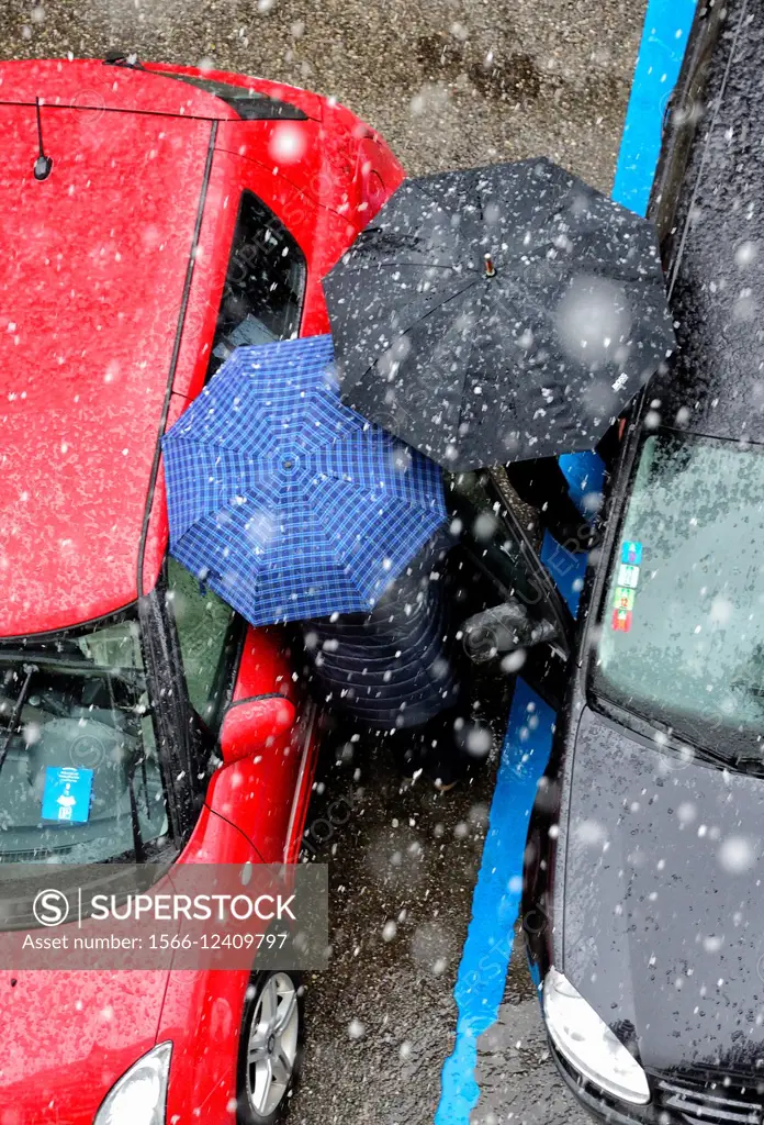 two persons under umbrellas in heavy snowfall trying to get into the car in parking lot, Geneva, Switzerland.