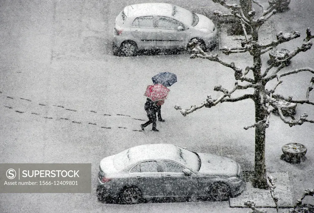 two persons under umbrellas in heavy snowfall, parking space, Geneva, Switzerland.