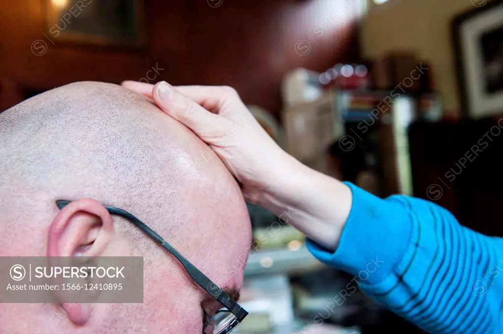 A woman´s hand rubbing a man´s bald head.