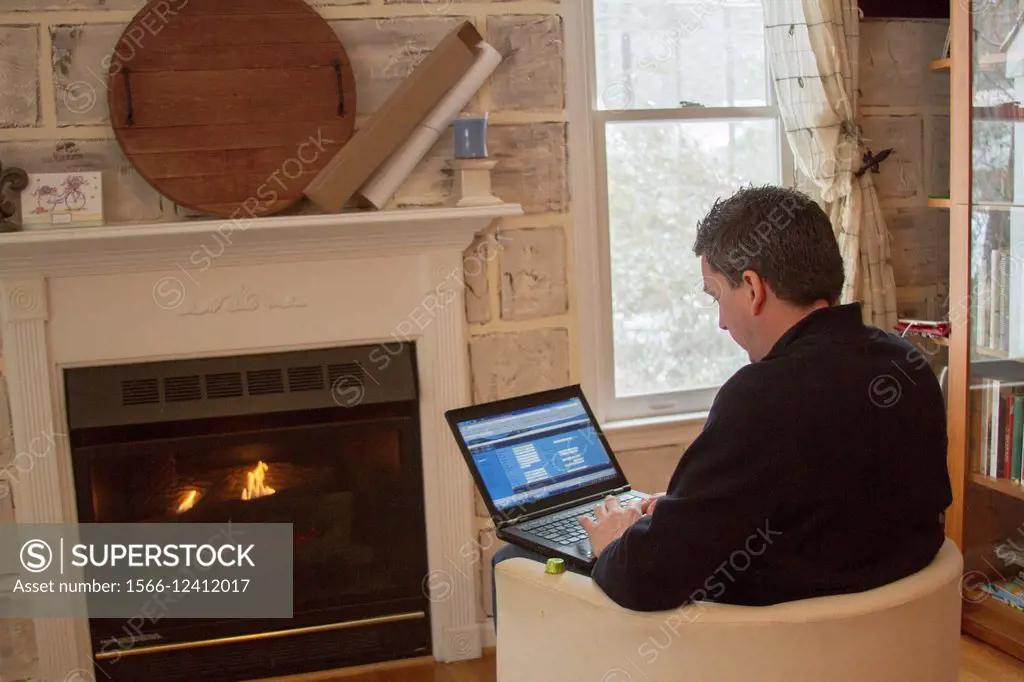 Caucasian man in his mid 40´s working on his laptop from home by the fireplace in a cold day in North Carolina during a snow storm.
