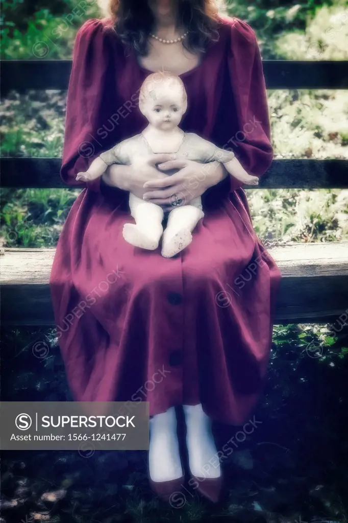 a woman in a red dress is sitting on a wooden bench with an old doll on her lap