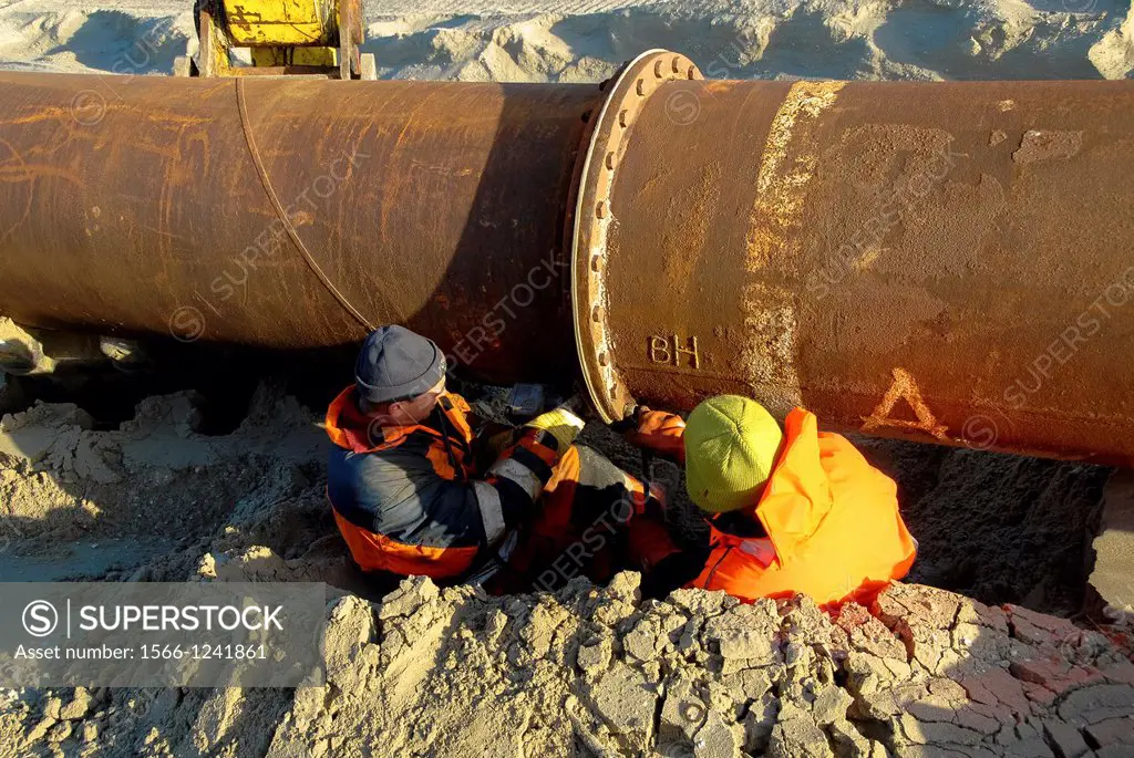 pipefitters at work at big pipe for sand supply at the beach in the Netherlands