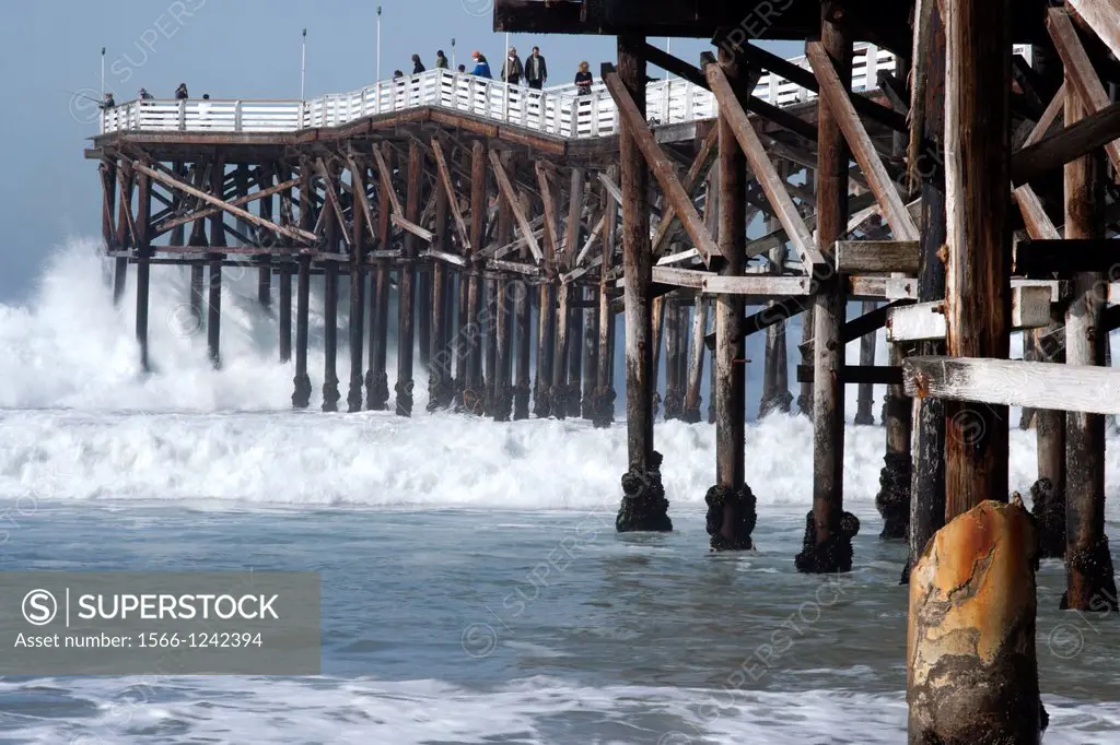 Pacific Ocean waves crash into a long, wood pier on the coast of San Diego, California.