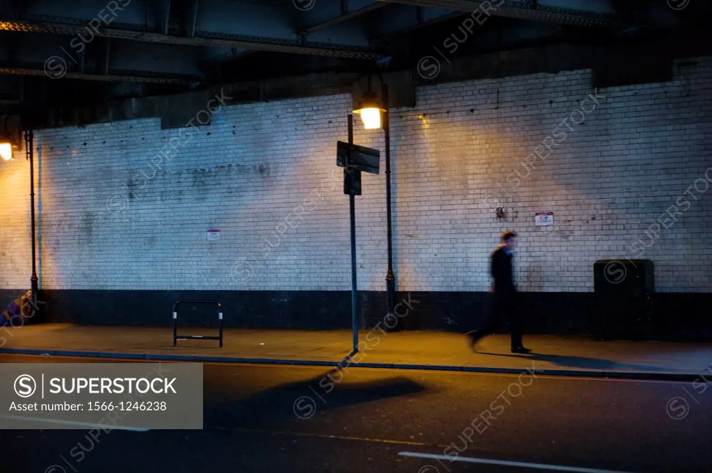 Loner walking under a bridge in the city, Kingsland Road Bridge, East London, England, UK