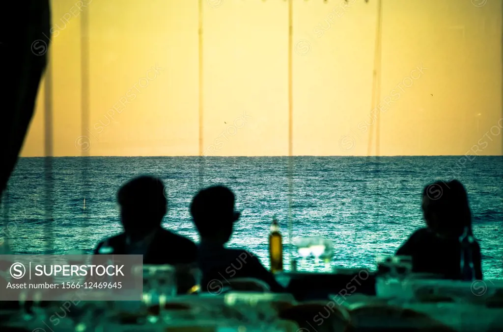 Silhouette of three people sitting near the sea and resting at sunset. Barcelona, Catalonia, Spain.
