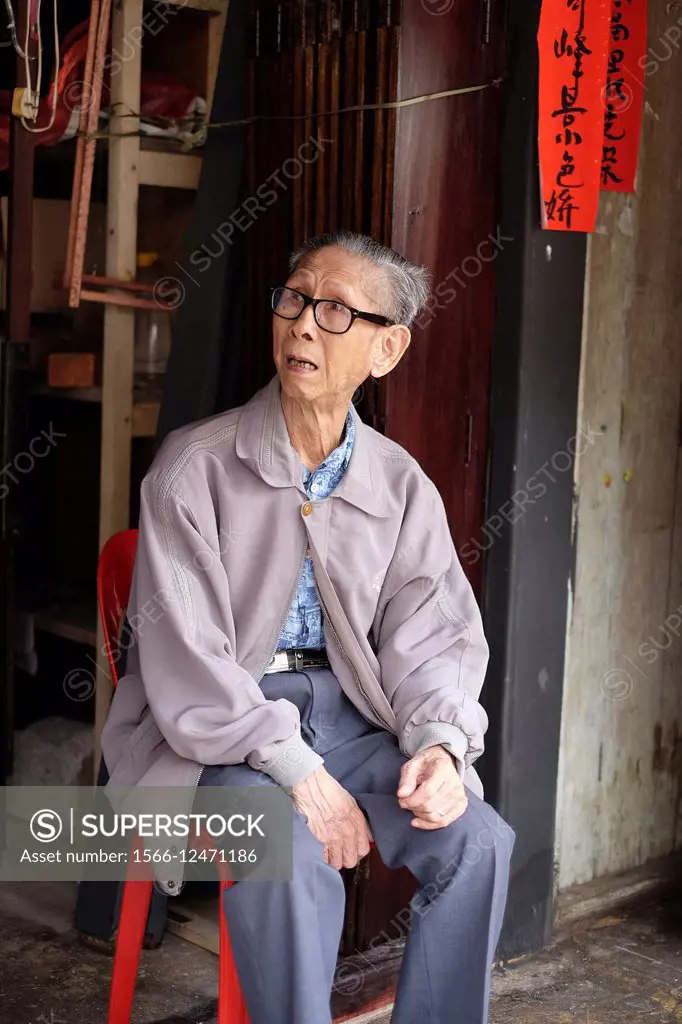 An elderly chinese man siting at the front door of Siniawan old town, Malaysia.