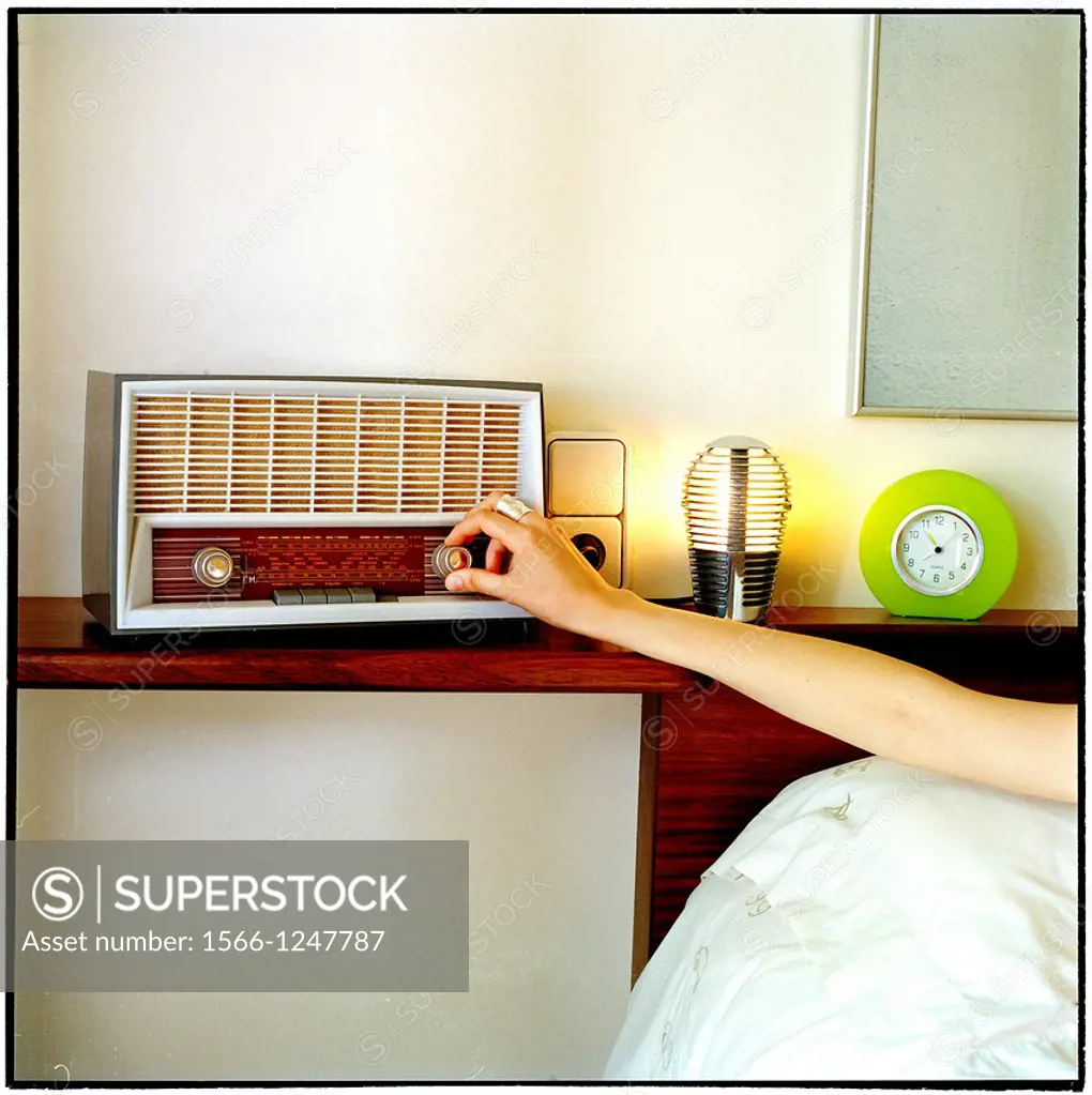 mano de persona encendiendo la radio desde la cama de un dormitorio, person´s hand turning the radio on from the bed of a bedroom