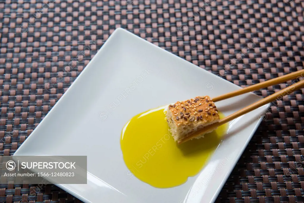 Chinese chopsticks dipping bread in olive oil. Close view.