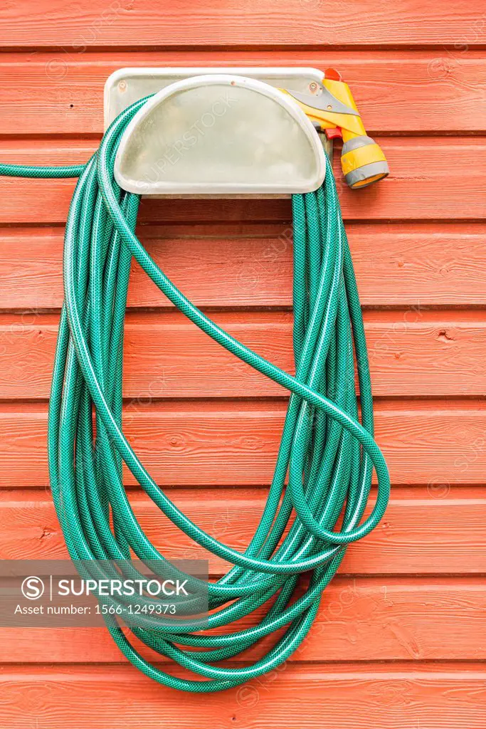 Green plastic garden hose and nozzle hanging the wall of a red wooden house