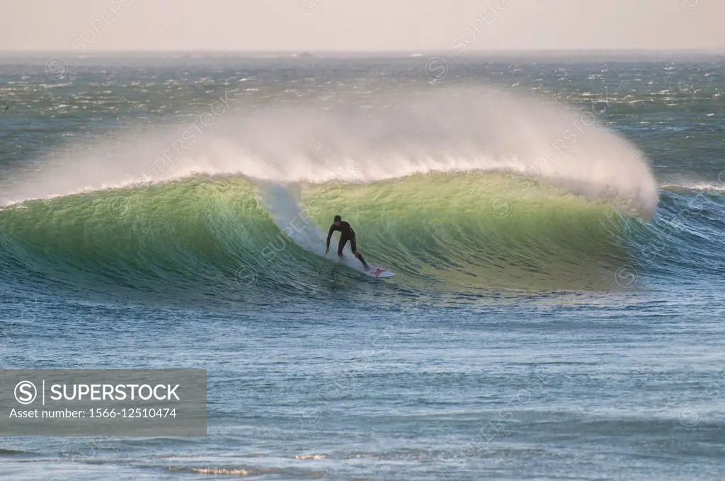 Illuminated water as sun strikes surf with surfer in action. Noord Hoek. South Africa.