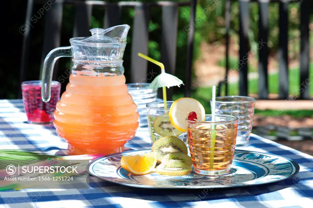 Jug with juice and matching glasses in outdoor setting