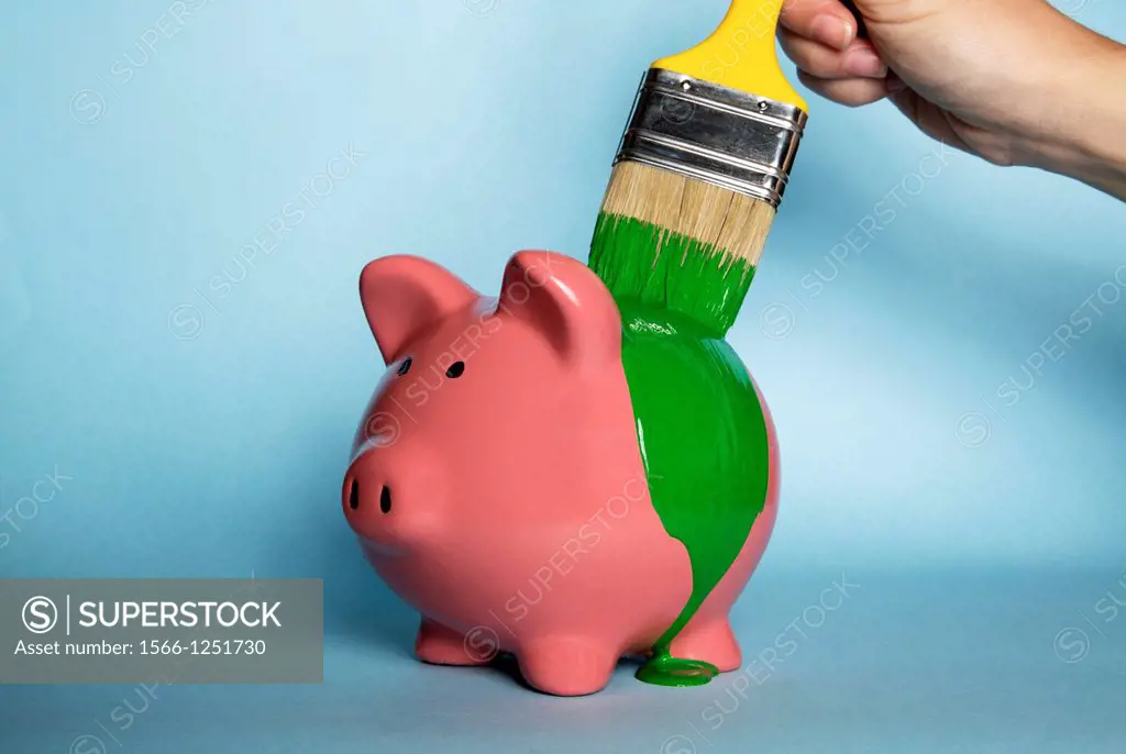 Woman´s hand painting a piggybank with green paint