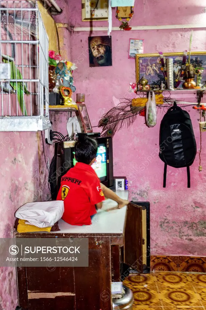 India, Asian, Mumbai, Dharavi, Kumbhar Wada, slum, high population density, poverty, low income, poor, resident, boy, home, watching tv television, in...