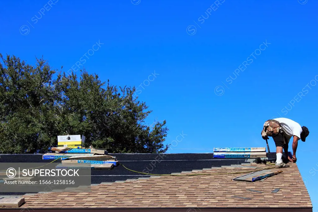 a man or roofer working to replace the shingles on a house roof