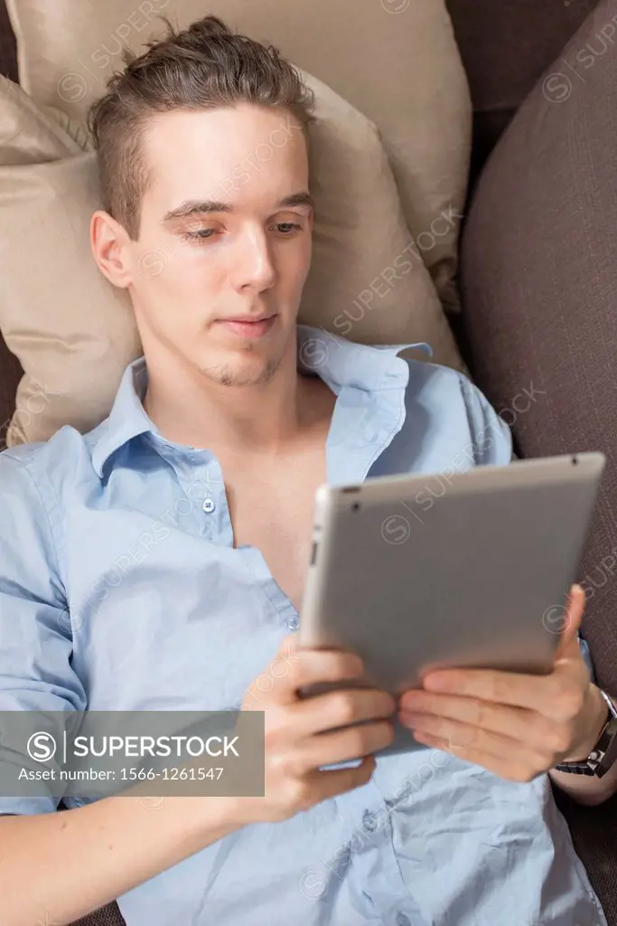Lifestyle moment with a relaxed young adult male holding a digital tablet device in his hands