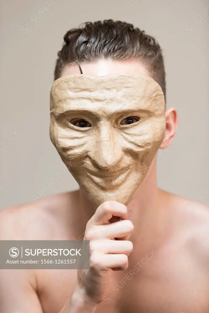 Portrait of a fragile and undressed young adult man hiding behind a happy mask