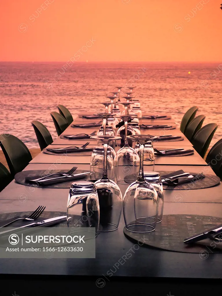 Table and chairs with cutlery and glasses near sea at sunset. Barcelona, Catalonia, Spain.