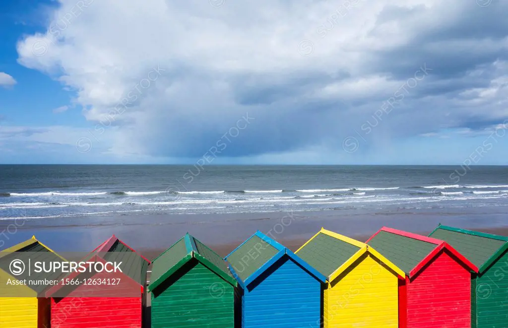 Whitby, North Yorkshire, England, United Kingdom. Europe. View over beach huts as storm clouds pass over North Sea.