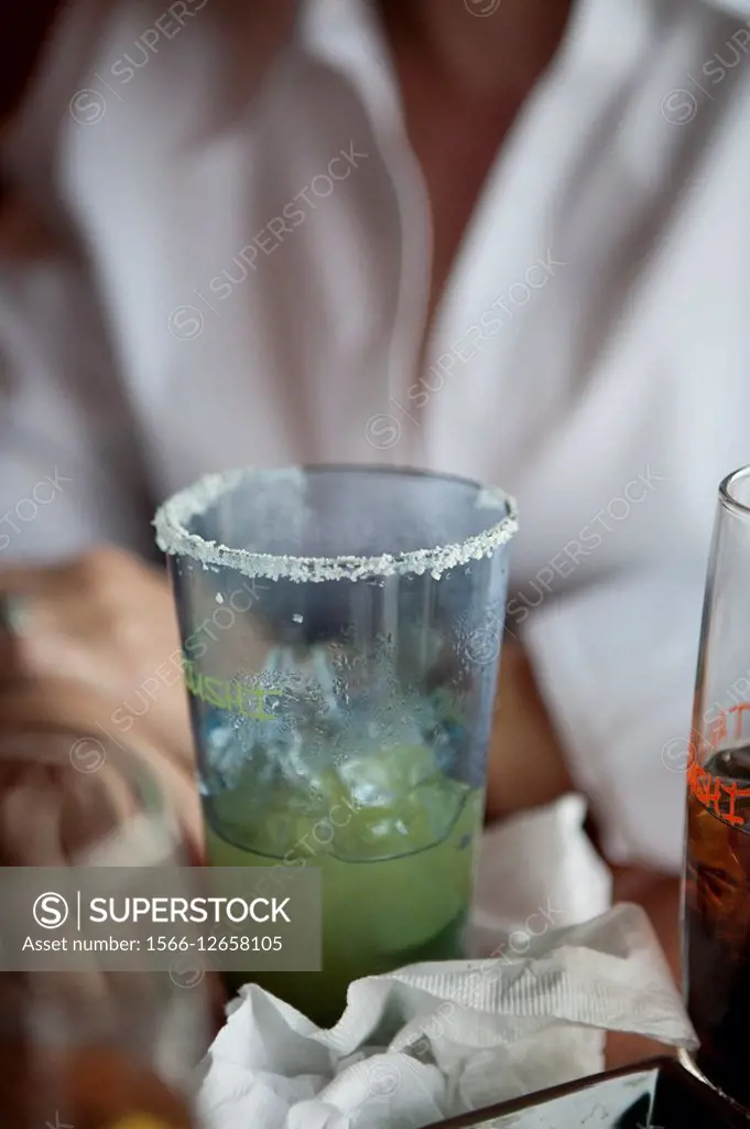 A partially empty alcoholic drink on a table in a restaurant with woman in background.