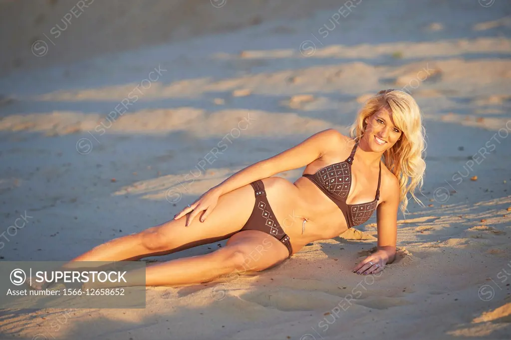 Young blond woman lying on a sandy beach in summer.