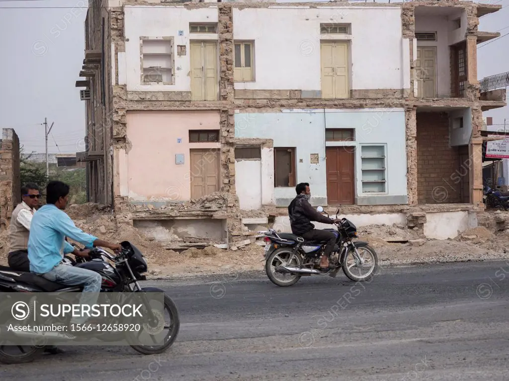 Men riding bike in front of ruined building cut to make way for highway expansion in Sojat, Pali district, Rajasthan, India