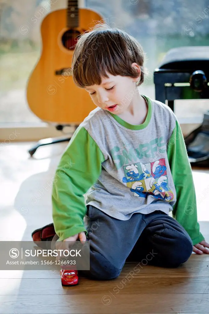 Boy playing alone indoor with a toy car.