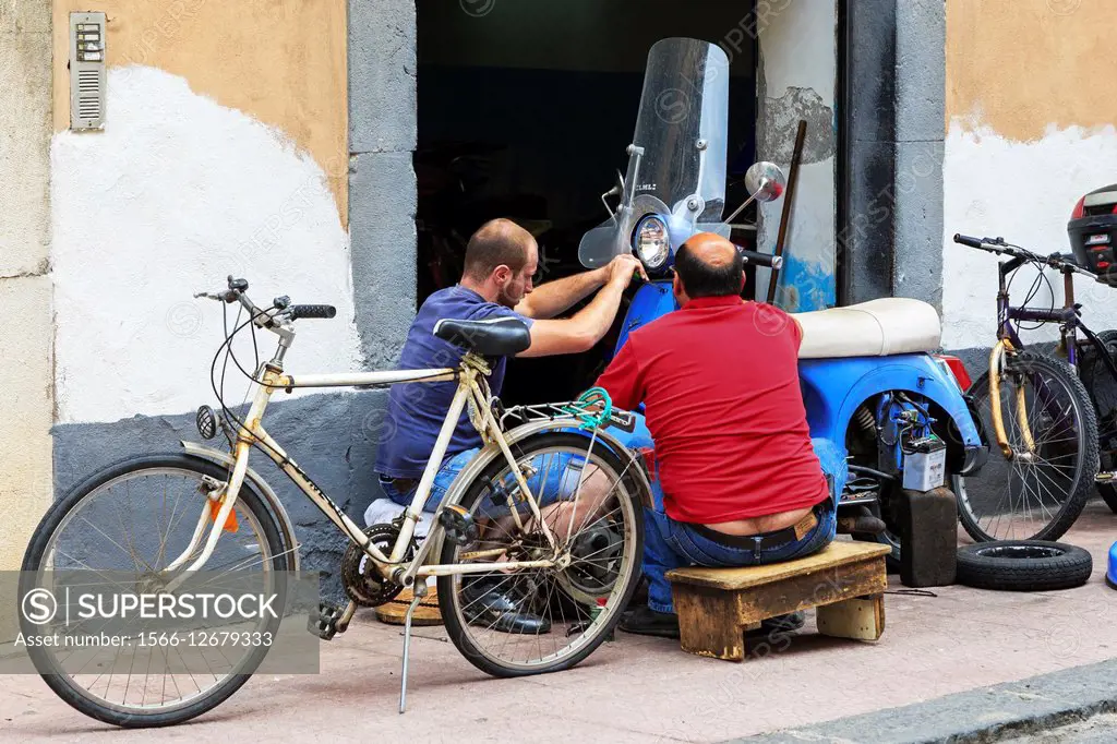 Two mechanics repairing a motorcycle, Giardini Naxos, Sicily, Italy.