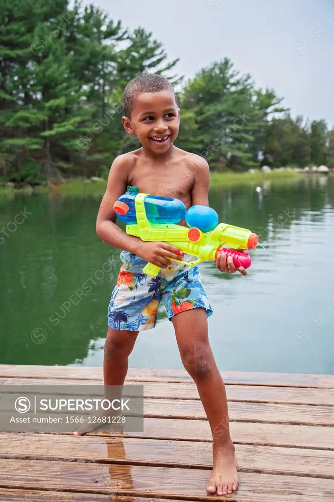 6 year old african american boy playing with fanciful water ´gun´ while standing on wooden dock in Gloucester, MA, mr_G110806_1.