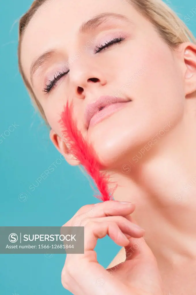 Beautiful young Caucasian woman feeling face with a red fether.