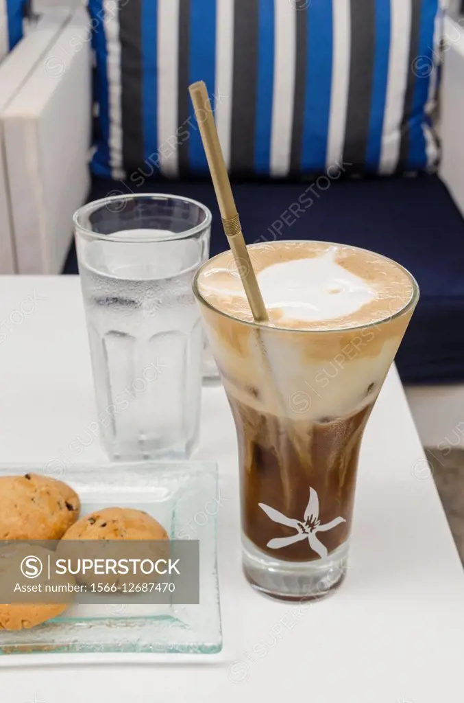 Iced coffee, a glass of water with some biscuits on a table in Greece.