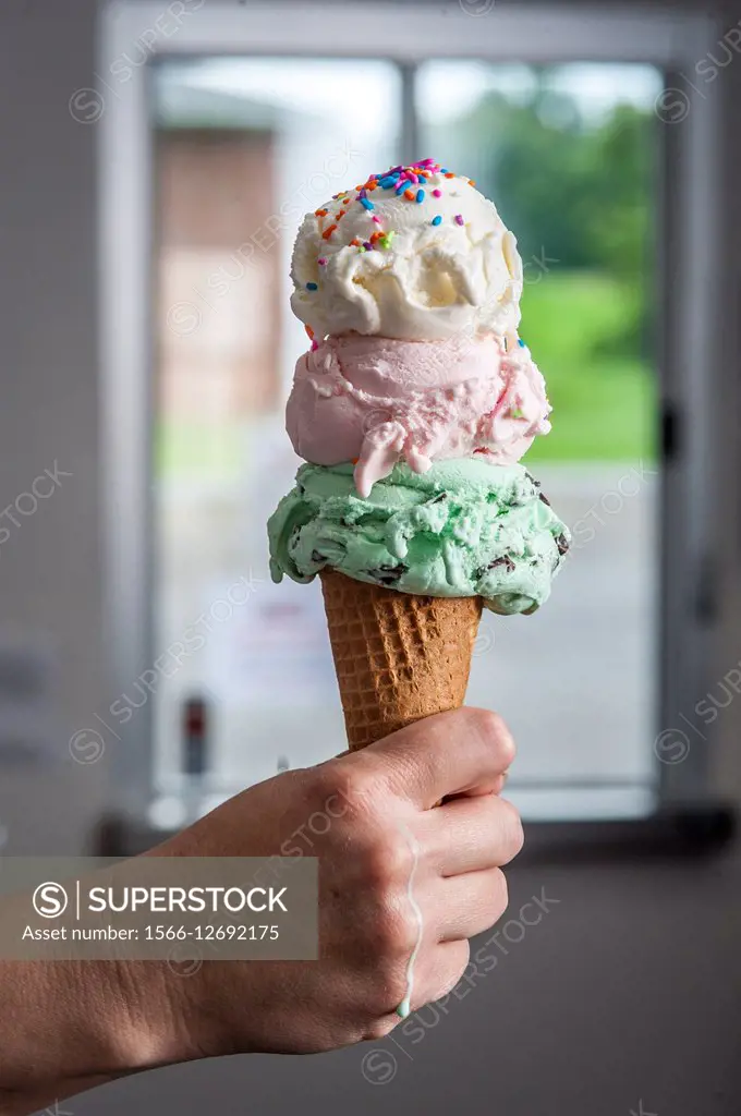 Hand holding a three scooped ice cream cone.