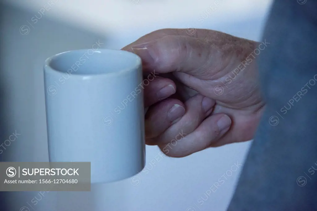 An older man holds his coffee cup.